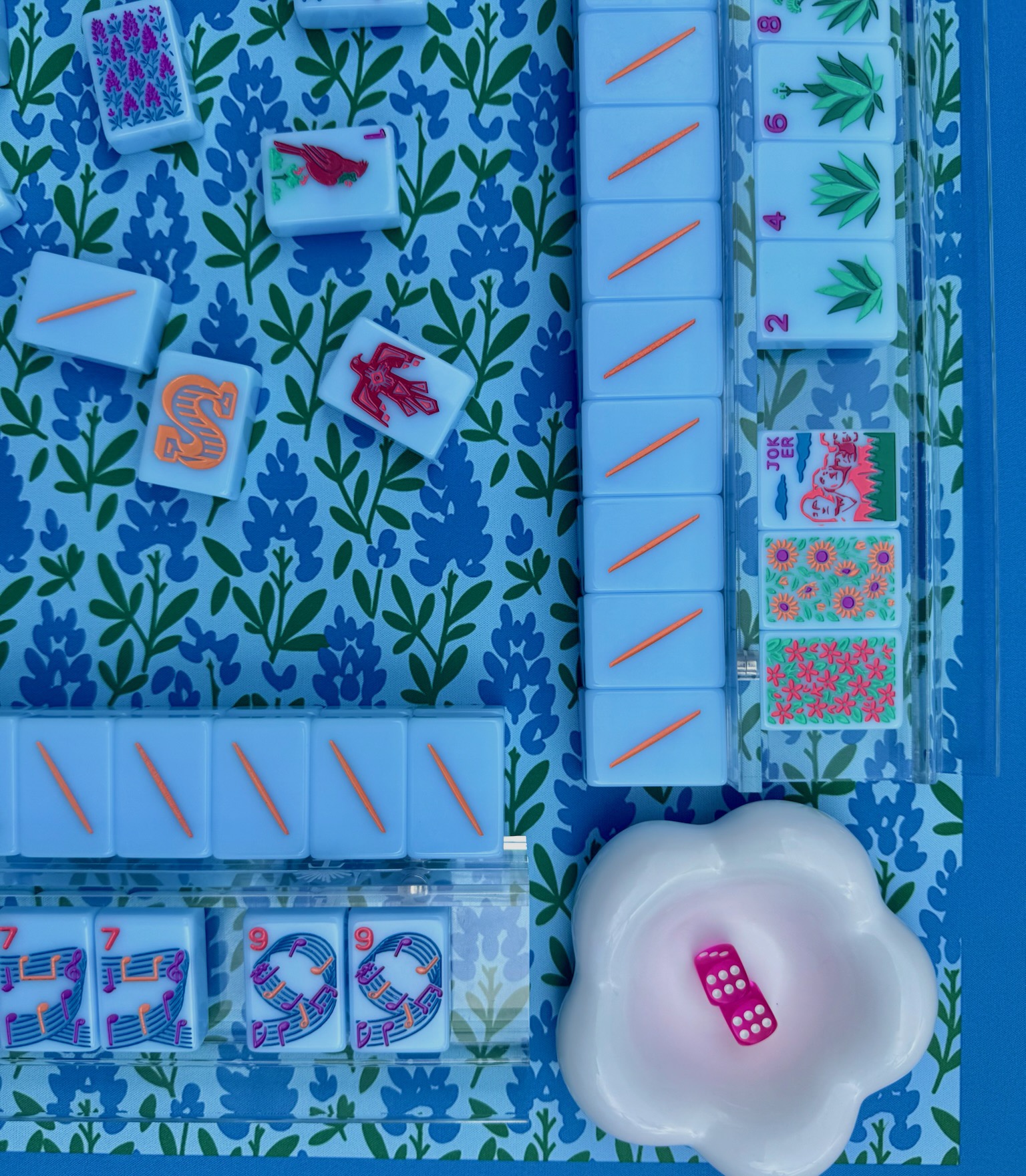 Pastel blue mahjong tiles and racks laid out on a floral mat